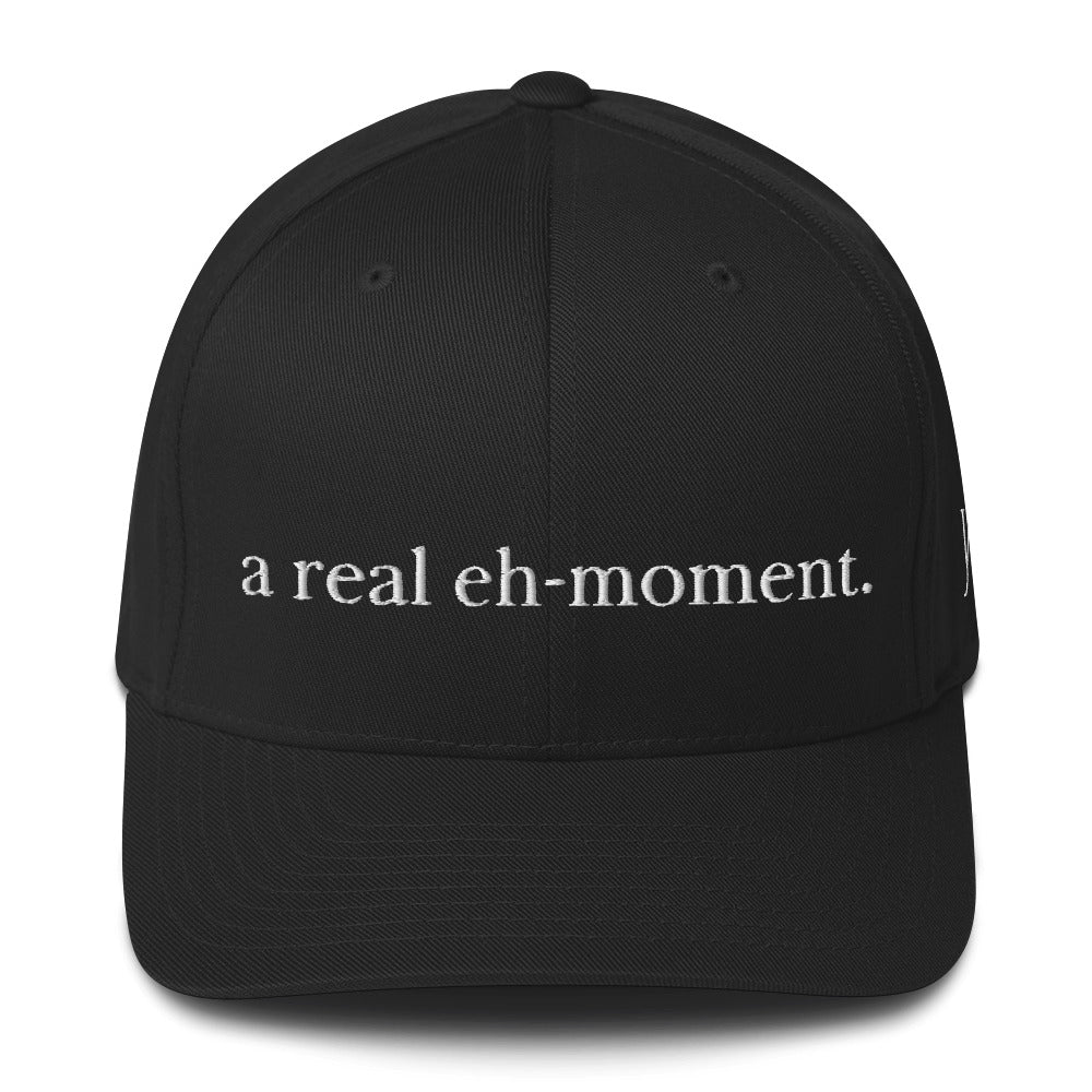 Classic Flexfit Yupoong black cap with the words "A Real Eh Moment" embroidered in white font at the front of the cap.