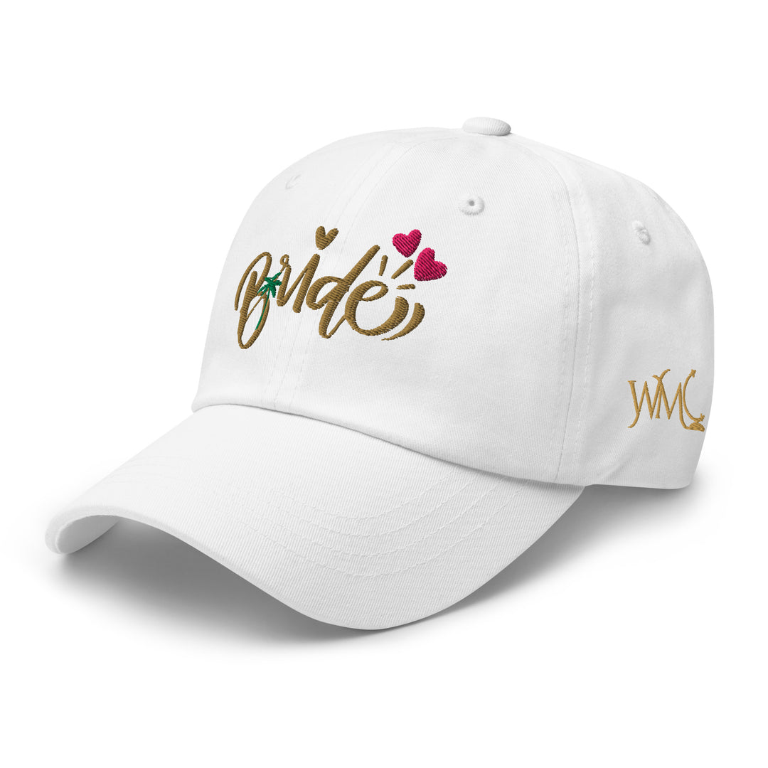 White classic cap with the word Bride embroidered in gold on the front. The design is accompanied by 3 hearts and a palm tree respresenting a tropical destination wedding.