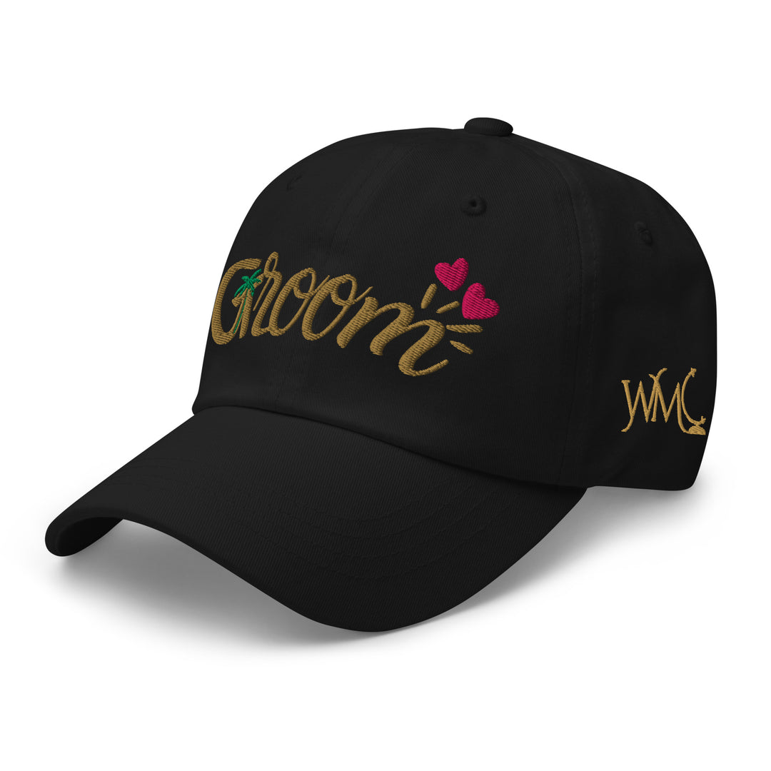 Classic cap with the word Groom embroidered on the front in gold font. The m in the word Groom is accentuated by two pink hearts. The letter G has a green palm tree representing tropical destination wedding vibes.