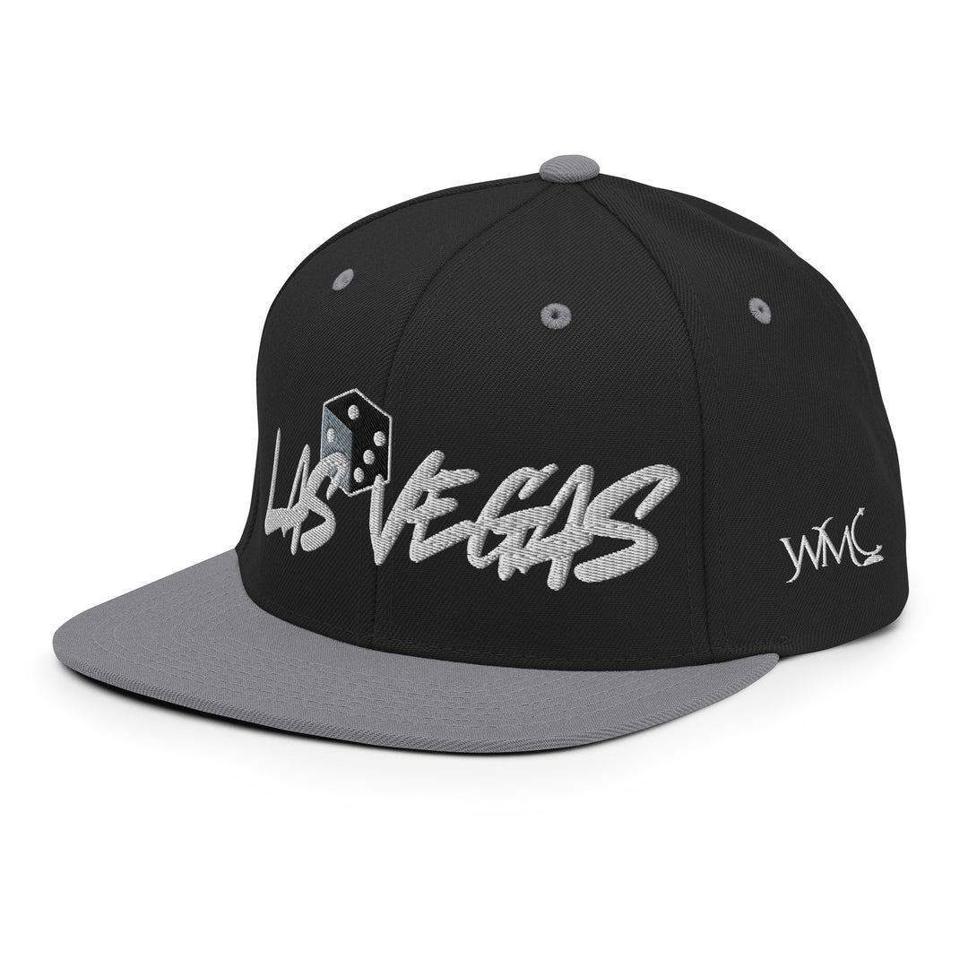 Black and gray snapback cap with the words LAS VEGAS embroidered on the front. The words LAS and VEGAS are separated by one die representing the casino culture.