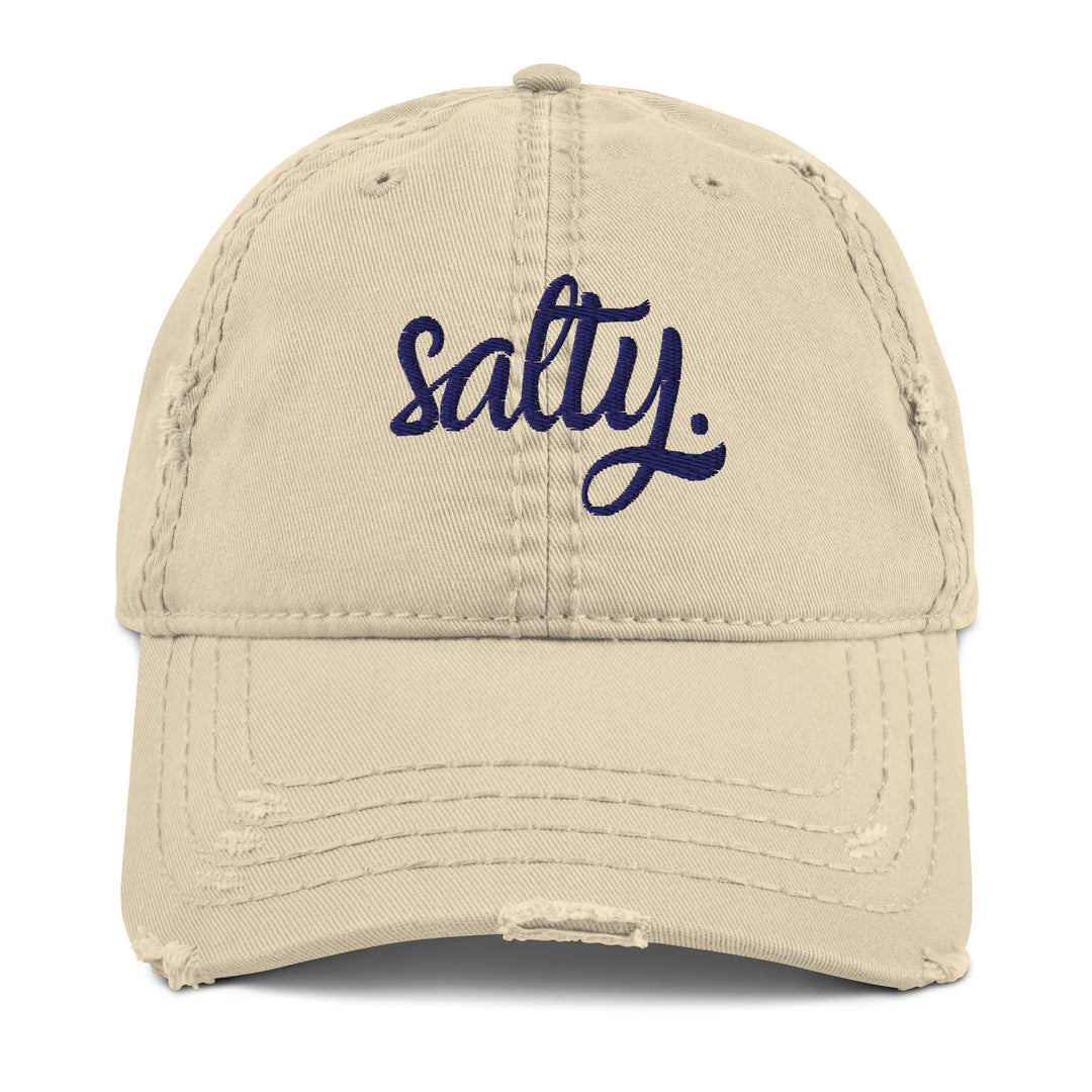 Beige cap with the word Salty embroidered in the front in cursive navy font. With its relaxed distressed finish and beige color reminiscent of sandy beaches, it pairs easily with any casual outfit, from beach walks to sunset drinks.