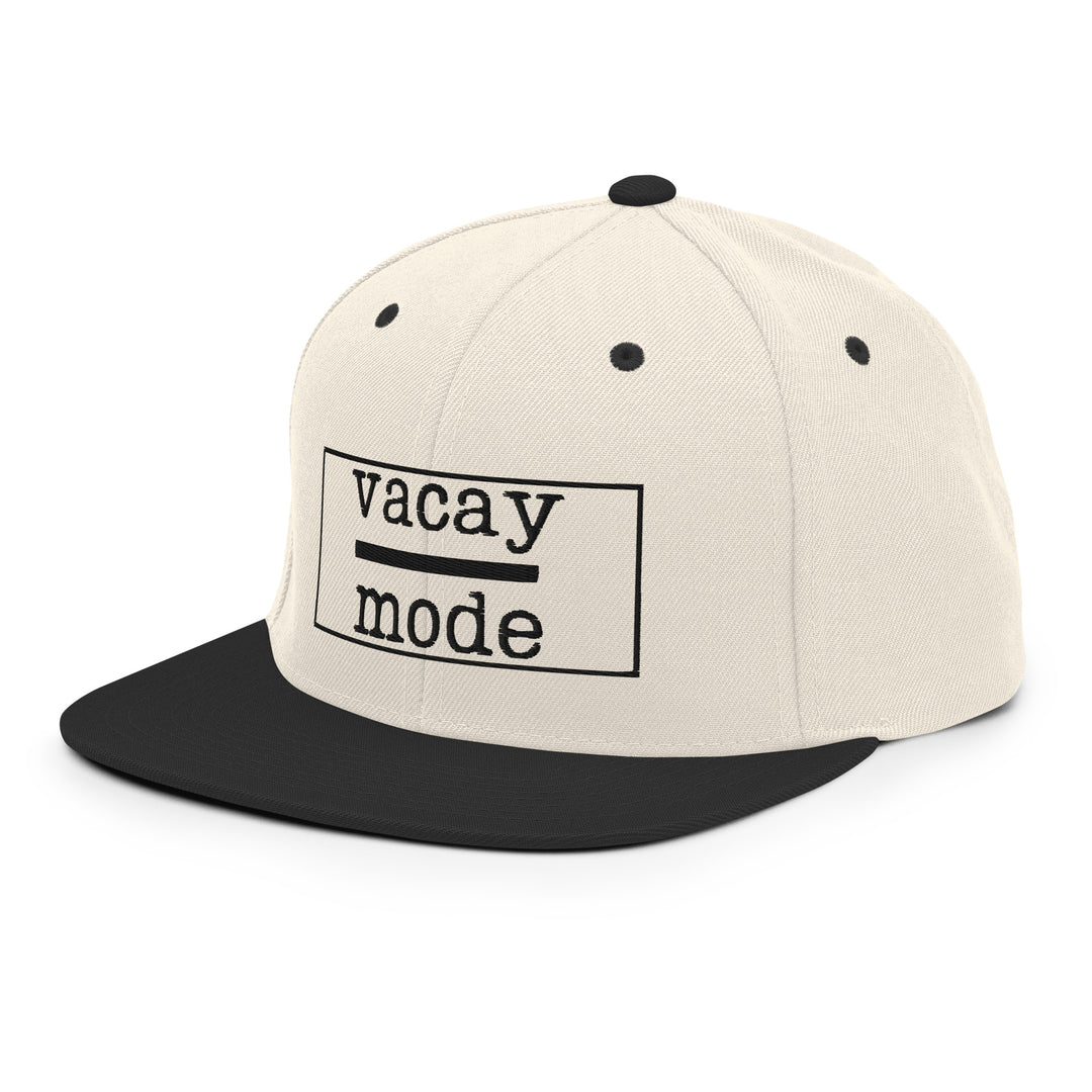 The cap features a clean beige crown with a black brim and snapback closure, creating a classic two-tone look that goes with just about any travel outfit. On the front, “Vacay Mode” is embroidered in bold black lettering, with “Vacay” stacked above “Mode” and separated by a sleek horizontal black line, giving the design a modern, minimalist travel vibe.