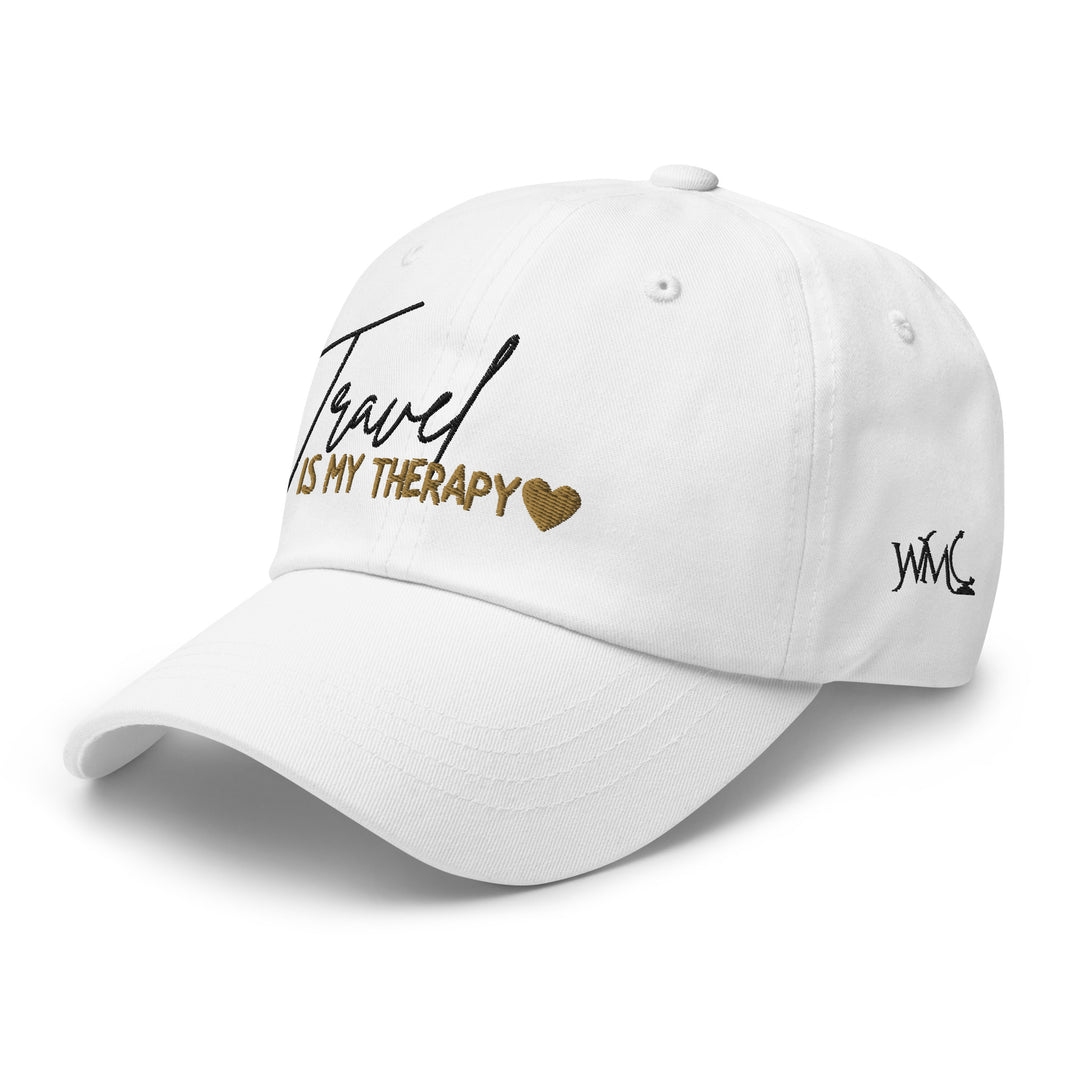 White classic cap with the words Travel Is My Therapy emboridered on the front. The word Travel is embroidered in black font while the words Is My Therapy are embroidered in gold font. At the end of the quote is a gold heart.